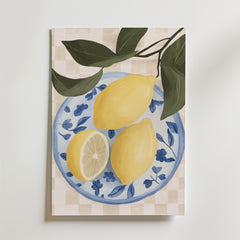 Bozetto Lemon Table Poster visar två hela citroner och en citronhalva på en blåvit blommig tallrik med gröna blad mot en beige rutig bakgrund, elegant tryckt på premium art paper.