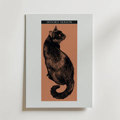 Bozetto Midnight Whiskers Poster föreställer en illustrerad svart katt med orange ögon på en brun bakgrund som tittar tillbaka under en "Spooky Season" banner. Med en vit kant är den perfekt för Halloween-dekoration eller magisk inredning.