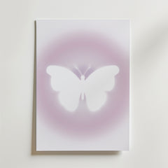Bozetto's Soft Glow Butterfly Poster visar en vit fjäril i silhuett centrerad mot en ljus, minimalistisk bakgrund med drömskt rosa-lila sken.