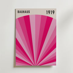 Bauhaus Pink Radiance Poster by Bozetto har "BAUHAUS" och "1919" högst upp, med geometriska rosa strålar som strålar ut från mitten på en ljus bakgrund, och kombinerar modern konst och klassisk design.