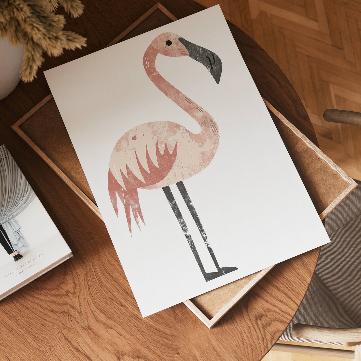 A minimalist illustration of no-9, a pink flamingo, is printed on a white sheet of paper resting on a wooden table next to a book and a potted plant.