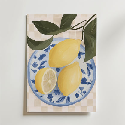 Bozetto Lemon Table Poster visar två hela citroner och en citronhalva på en blåvit blommig tallrik med gröna blad mot en beige rutig bakgrund, elegant tryckt på premium art paper.
