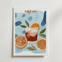 Bozetto Negroni No.3 Drink Poster visar ett glas Negroni med is, apelsinskivor och gröna blad på en blå akvarellbakgrund. "Negroni" står högst upp i orange skrift, tryckt på premiumpapper.