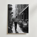 Charming Street Café Poster från Bozetto visar en svartvit scen av ett livligt utomhuscafé med gäster, en servitör och cyklar på en kullerstensgata - perfekt att visa på premiumpapper.