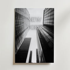 Bozetto New York Poster föreställer svartvita skyskrapor tagna från en låg vinkel med "NEW YORK" i transparenta bokstäver, tryckt på FSC-certifierat premiumpapper för en miljövänlig touch.