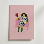 På postern Wine Down Poster från Bozetto syns en minimalistisk kvinna med mörkt hår i en mönstrad klänning och gröna boots, som slappnar av i en rosa stol med rödvin mot en rosa bakgrund. Tryckt på premiumpapper - perfekt för stilfulla inredningar.