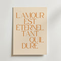 Postern Lamour Est Eternel Tant Quil Dure Poster från Bozetto har orange fransk text på beige, tryckt på premiumpapper med en lyxig matt yta för en sofistikerad look - perfekt för att lyfta alla utrymmen.