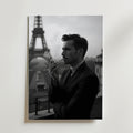 En man i kostym röker på en balkong med Eiffeltornet i bakgrunden. Bozetto Parisian Elegance Poster har en klassisk, stämningsfull stil - perfekt för att ge sofistikerad parisisk charm till alla rum.