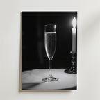 Ett glas mousserande champagne och ett tänt ljus står på ett runt bord i mjukt, stämningsfullt ljus och återspeglar elegansen i Bozettos Champagne Dinner Poster - det perfekta tillskottet till alla sofistikerade middagar.