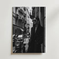Noire Elegance Fashion Poster från Bozetto visar en elegant kvinna i lång rock och solglasögon som lutar sig på en motorcykel mot stadens skyskrapor. Den svartvita designen erbjuder en högkvalitativ finish för tidlös elegans.