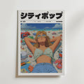 Neon Beach Dreams Poster av Bozetto visar ett tidningsomslag i japansk stil med en kvinna i solglasögon och sommarkläder på en strand bland retroföremål som väcker 80-talsnostalgi. "シティポップ" (City Pop) står med stora bokstäver högst upp.