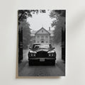 En klassisk svart Vintage Rolls Royce glider genom järngrindar mot en stor herrgård en dimmig dag, omgiven av träd - en idealisk scen på Bozetto Vintage Rolls Royce Poster, tryckt på premiumpapper med matt yta.