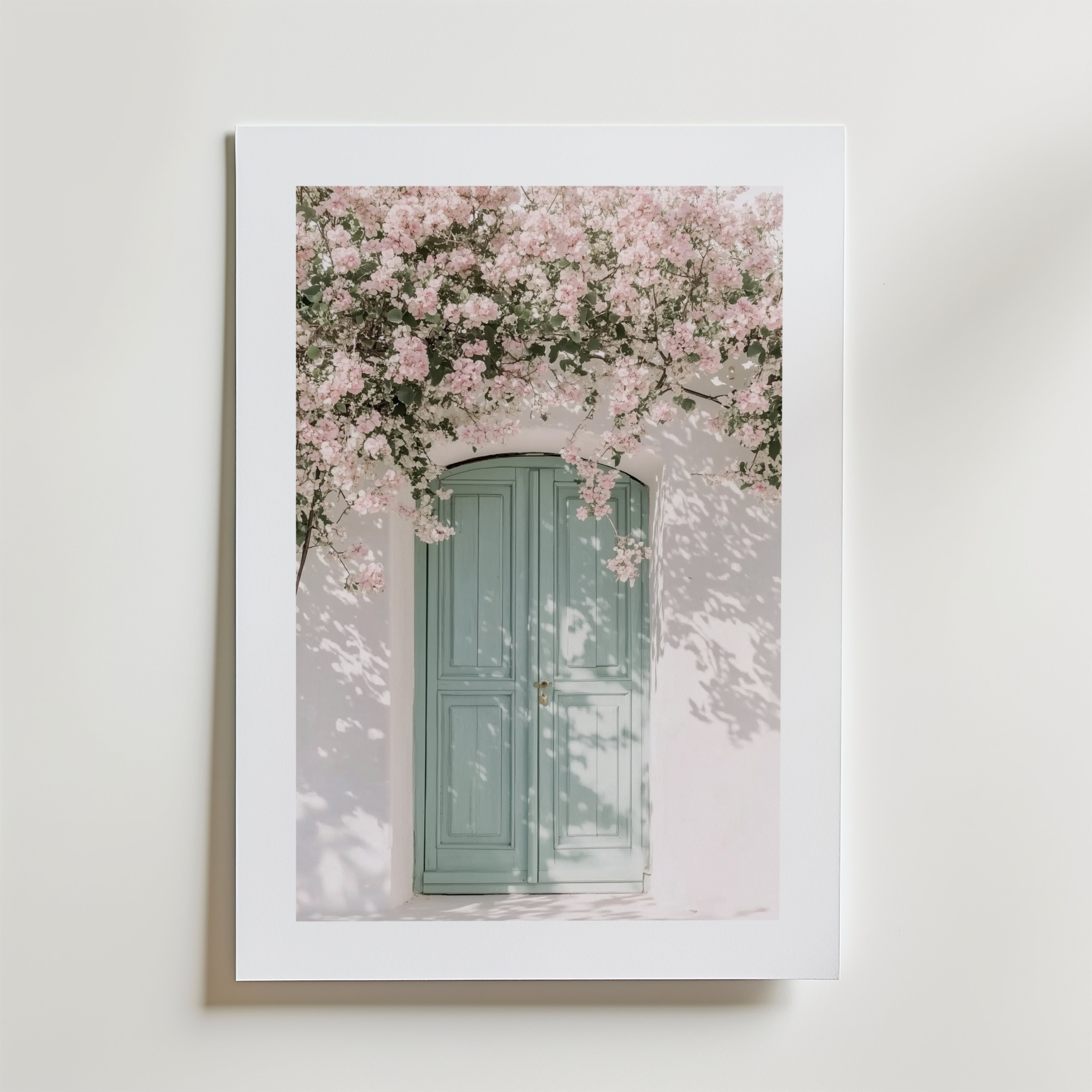 Blossom & Mint Poster by Bozetto föreställer en pastellfärgad dörr i en vit vägg under rosa körsbärsblommor. Tryckt på FSC-certifierat premiumpapper för en högkvalitativ finish och lyxigt matt yta.