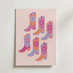 Bozetto Pink Cowboy Boots Poster har sex livfulla, blommiga cowboyboots i rosa, lila, orange och rött på en ljusrosa bakgrund - perfekt för att skapa en rolig westernkänsla i alla rum.