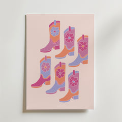 Bozetto Pink Cowboy Boots Poster har sex livfulla, blommiga cowboyboots i rosa, lila, orange och rött på en ljusrosa bakgrund - perfekt för att skapa en rolig westernkänsla i alla rum.