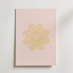 Golden Bloom on Blush Poster by Bozetto är en minimalistisk konstprint med ett guldgult, blomliknande mönster av detaljerade bladliknande kronblad på ljusrosa, som visas på en ljus yta.