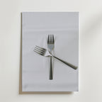 Två metallgafflar korsade i en X-form vilar på en vit tygservett ovanpå en vit yta - en elegant komposition som visas på Bozetto Classic Forks Poster.