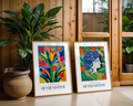 Två inramade Bozetto Bundle 2-pack Henri Matisse No. 2 konsttryck vilar på golvet mot en trävägg, bredvid stora krukväxter och en spegel som reflekterar grönska i ett mysigt, solbelyst rum.
