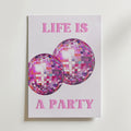 Life Is a Party Poster by Bozetto föreställer två glänsande lila och rosa discobollar med den rosa frasen "LIFE IS A PARTY" på en vit bakgrund.